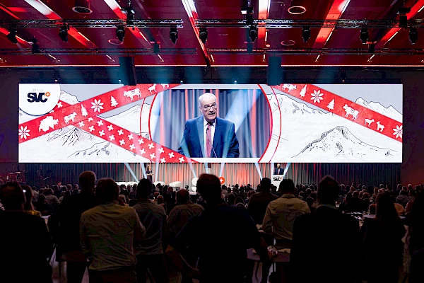 Eventfotograf Festhalle Bern: Redner auf der Bühne, live auf der Grossleinwand mit Wintermotiv übertragen – Gäste verfolgen die Präsentation